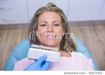 Dentist holding tooth whitening equipment by smiling patient at clinic 36835501