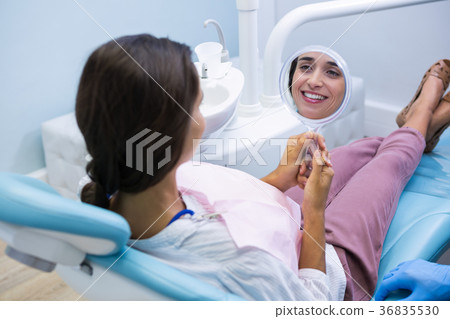 Woman looking at mirror while sitting on dentist chait at clinic Woman looking at mirror while sitting on dentist chait at clinic 36835530