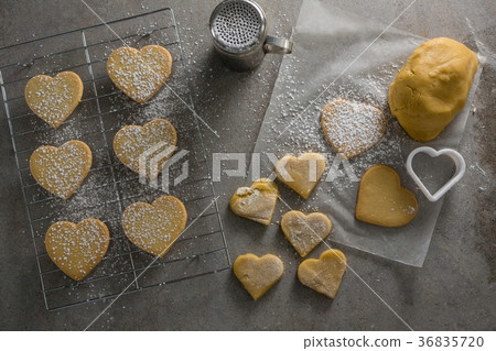 Raw heart shape cookies on baking tray with flour shaker strainer, cookie cutter and wax paper Raw heart shape cookies on baking tray with flour shaker strainer, cookie cutter and wax paper 36835720