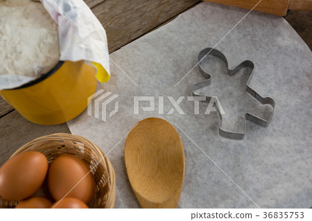 Butter paper, flour, rolling pin cookie cutter and eggs kept over a wooden table 36835753