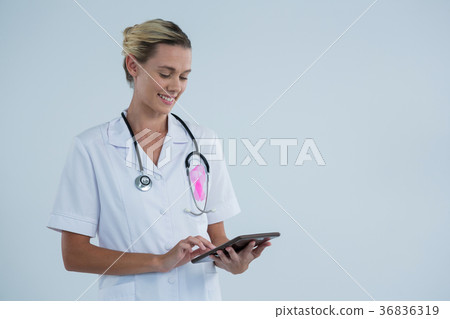 Smiling female doctor with Breast Cancer Awareness ribbon using tablet computer Smiling female doctor with Breast Cancer Awareness ribbon using tablet computer 36836319
