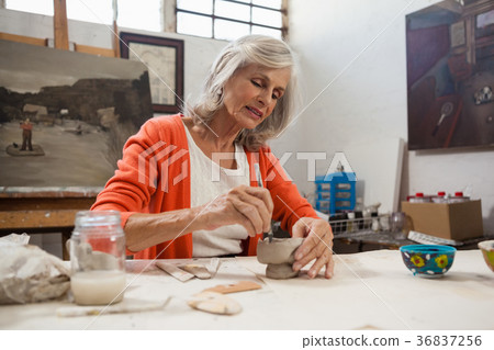 Attentive senior woman shaping a clay pot 36837256