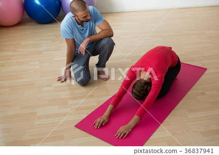 Instructor guiding student in doing child pose at yoga studio 36837941