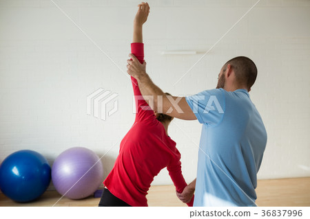 Rear view of instructor assisting student in exercising at health club 36837996