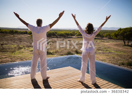 Rear view of couple standing with arms outstretched near poolside 36838342
