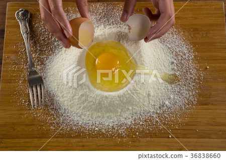 Man breaking eggs in the flour on wooden board Man breaking eggs in the flour on wooden board 36838660