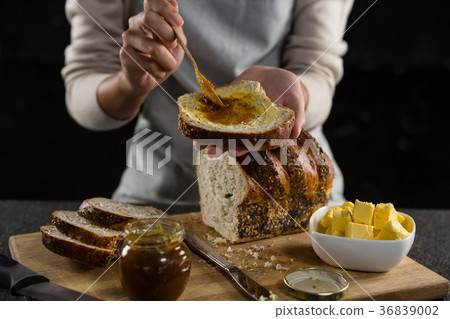 Woman applying jam over multigrain bread slice 36839002