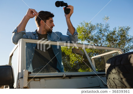 young man holding binoculars looking away while standing in off road vehicle young man holding binoculars looking away while standing in off road vehicle 36839361