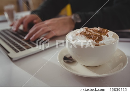 Cropped hands of businessman using laptop by coffee cup Cropped hands of businessman using laptop by coffee cup 36839513