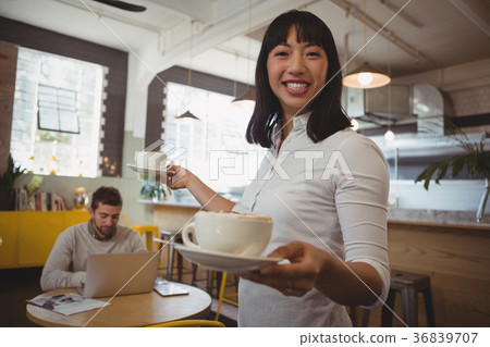 Portrait of waitress holding coffee cups with man using laptop at table 36839707
