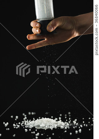 Mans hand sprinkling sea salt against black background Mans hand sprinkling sea salt against black background 36840066