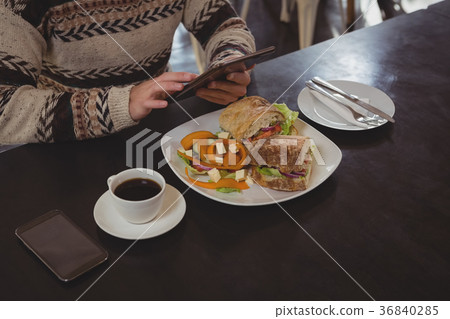 Mid section of man with breakfast using digital tablet in cafe Mid section of man with breakfast using digital tablet in cafe 36840285