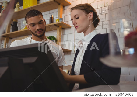 Female owner with waiter using cash register in cafe 36840405
