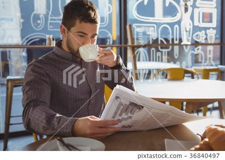 Businessman reading newspaper while drinking coffee in cafe Businessman reading newspaper while drinking coffee in cafe 36840497