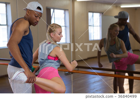 Man assisting female friend in stretching leg on barre Man assisting female friend in stretching leg on barre 36840499