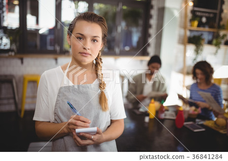 Confident young waitress standing with notepad at cafe Confident young waitress standing with notepad at cafe 36841284