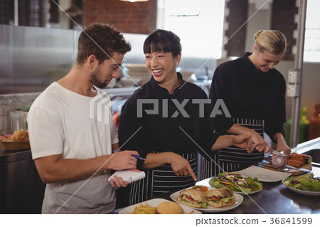 Cheerful chef pointing at food to waiter by female colleague Cheerful chef pointing at food to waiter by female colleague 36841599