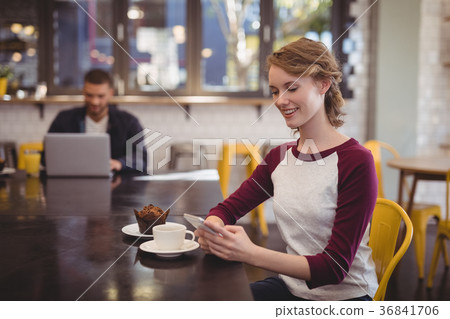 Smiling young woman using smartphone while sitting at cafeteria 36841706