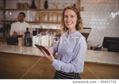 Smiling young waitress using digital tablet while standing by counter 36841738