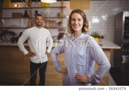 Smiling young woman with hand on hip against friend at coffee shop Smiling young woman with hand on hip against friend at coffee shop 36842079