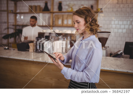 Young pretty waitress using digital tablet while standing by counter Young pretty waitress using digital tablet while standing by counter 36842197