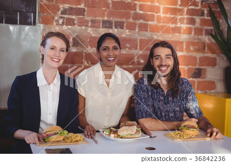 Portrait of smiling young friends sitting with food against brick wall 36842236