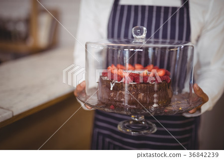 Midsection of waiter holding fresh cake on glass cakestand 36842239