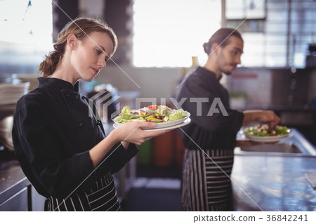 Young wait staff holding fresh salad plates while standing in commercial kitchen Young wait staff holding fresh salad plates while standing in commercial kitchen 36842241
