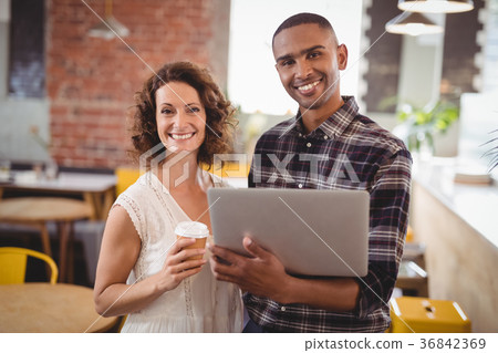 Smiling young friends standing with disposable coffee cup and laptop 36842369