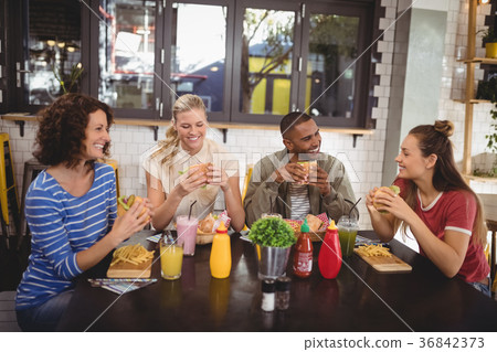 Smiling young friends eating food while sitting at coffee shop Smiling young friends eating food while sitting at coffee shop 36842373