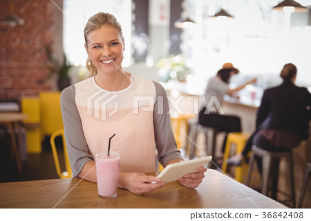 Portrait of smiling young blond woman sitting with tablet and milkshake 36842408