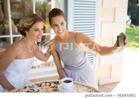 Bridesmaid taking selfie with bride in yard 36845802