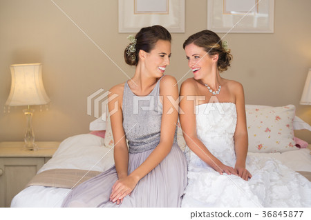 Happy bride and bridesmaid while sitting on bed at home 36845877