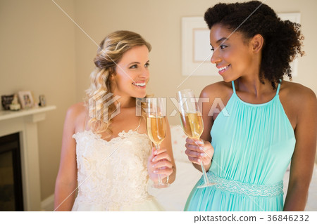 Happy bride and bridesmaid toasting drinks at home 36846232