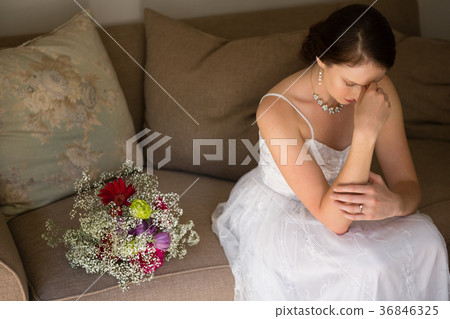Sad bride sitting by bouquet on sofa at home 36846325