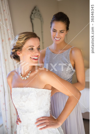 Happy bridesmaid adjusting bride wedding dress in room 36846345