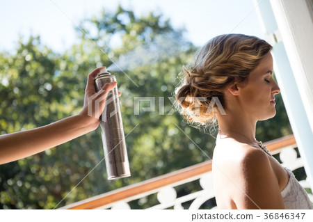 Bridesmaid applying hairspray to bride in dressing room 36846347