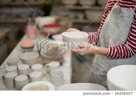 Mid section of female potter holding stack of bowls 36846887