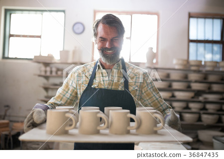Happy male potter holding ceramic cups in tray Happy male potter holding ceramic cups in tray 36847435