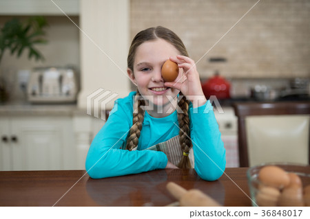 Girl holding egg while sitting on table in the kitchen 36848017