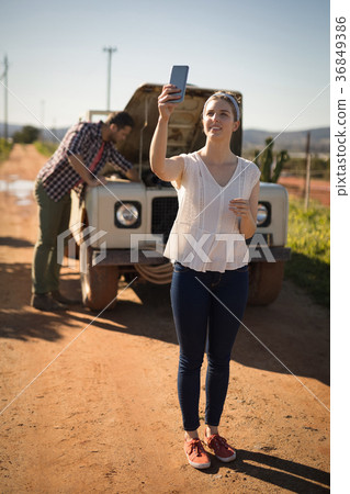 Woman taking selfie with mobile phone while man repairing a car Woman taking selfie with mobile phone while man repairing a car 36849386