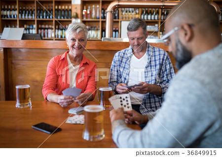Happy friends playing cards while having glass of beer Happy friends playing cards while having glass of beer 36849915