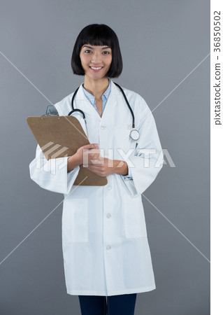 Doctor holding clipboard against grey background Doctor holding clipboard against grey background 36850502