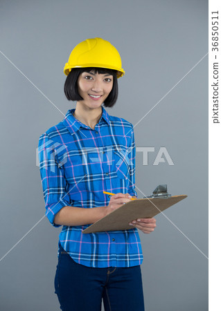 Female architect writing on clipboard against grey background Female architect writing on clipboard against grey background 36850511