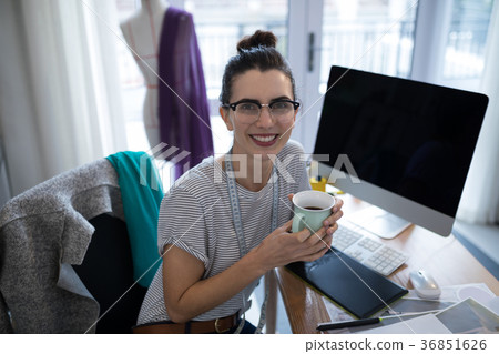 Smiling female designer having coffee at desk Smiling female designer having coffee at desk 36851626