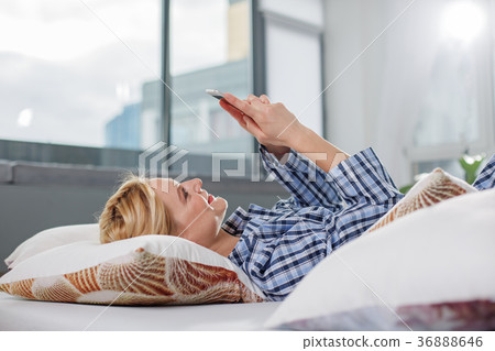Woman in bed looking at smartphone with smile 36888646