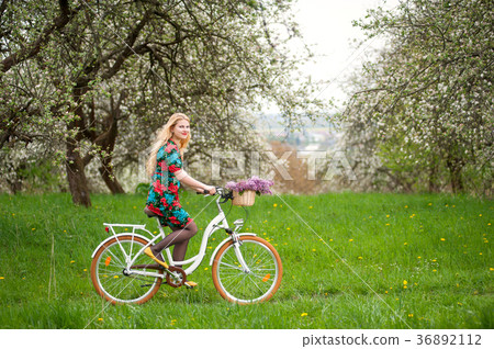 Woman riding vintage white bicycle with flowers basket 36892112