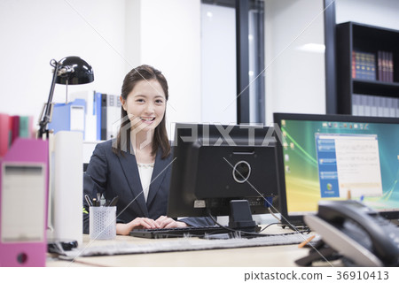 研究一台個人計算機的年輕女性僱員在工作,看照相機 研究一台個人計算機的年輕女性僱員在工作,看照相機 36910413
