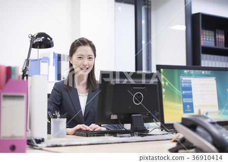 研究一台個人計算機的年輕女性僱員在工作,看照相機 研究一台個人計算機的年輕女性僱員在工作,看照相機 36910414
