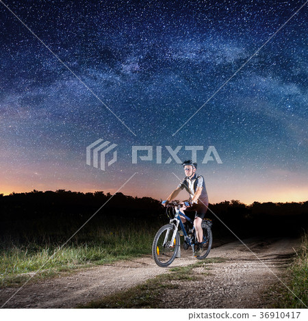Cyclist riding bike in the night under starry sky Cyclist riding bike in the night under starry sky 36910417